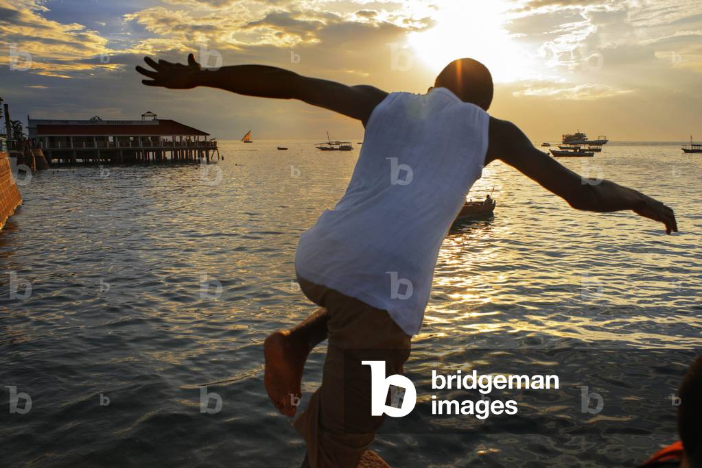 Local boys jumping off the Malecon into the sea next to the pier in Stone Town, Zanzibar, Tanzania, Africa (photo)