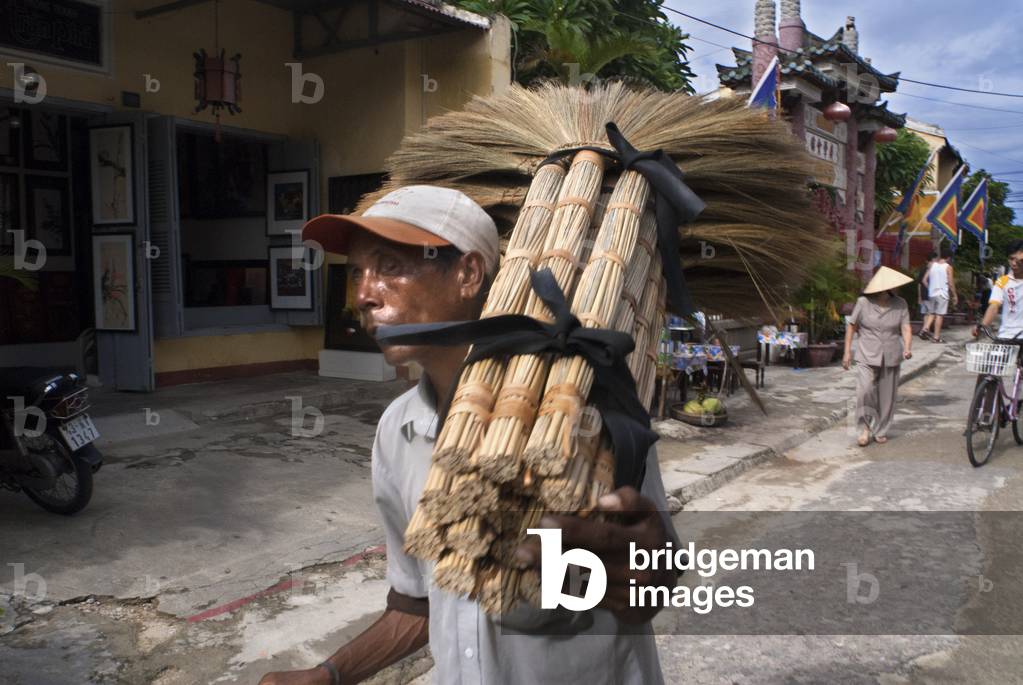 A local vietnamese man in Hoi An old town with a load of brooms, Vietnam (photo)