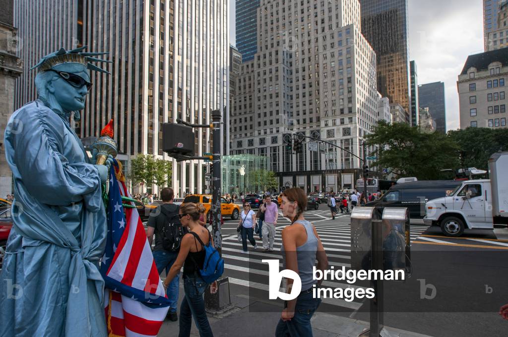 A human statue dressed in Statue of Liberty with tourists waiting to be photographed at the exit of Central Park plaza overlooking the Grand Army Plaza, New York City, USA (photo)