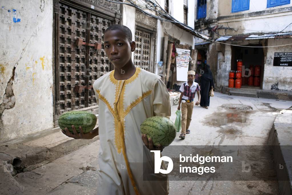 Man with a two water melons next to the massive teak doors of one house in Stone Town s maze of narrow streets, Zanzibar, Tanzania, Africa (photo)
