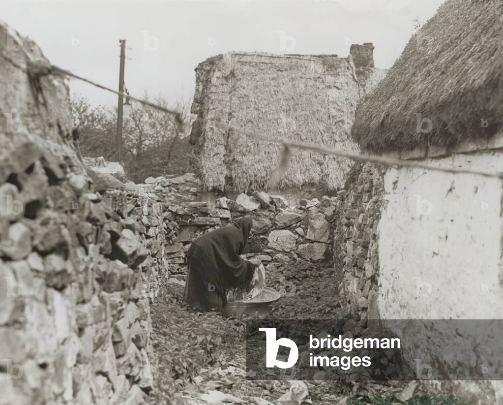 Woman washing clothes in the open air with rainwater, Claddagh, Galway, Ireland, c.1930 (b/w photo)