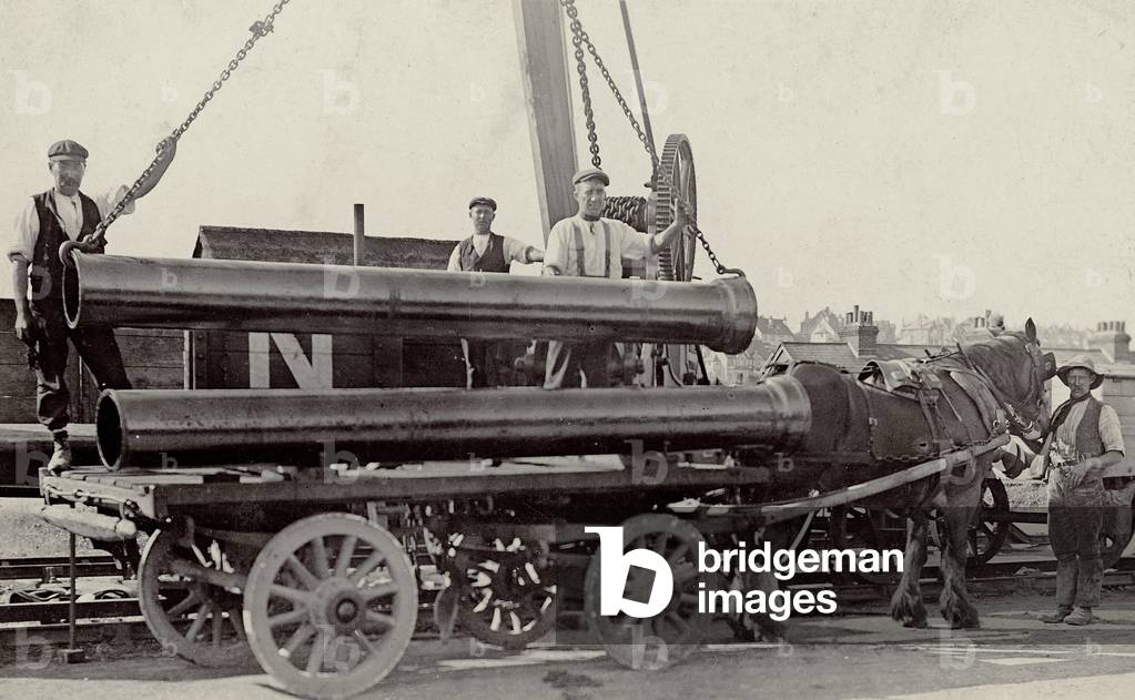 Workers transporting metal pipes or columns, late 19th / early 20th century (b/w photo)
