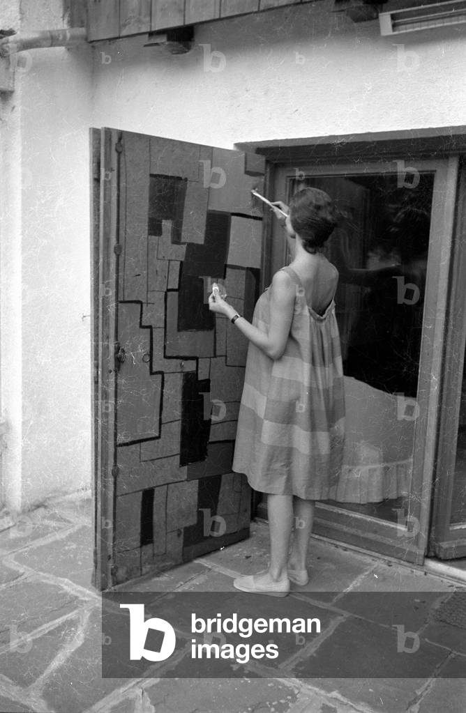 Simone Bicheron painting a wooden door, 1959 (b/w photo)