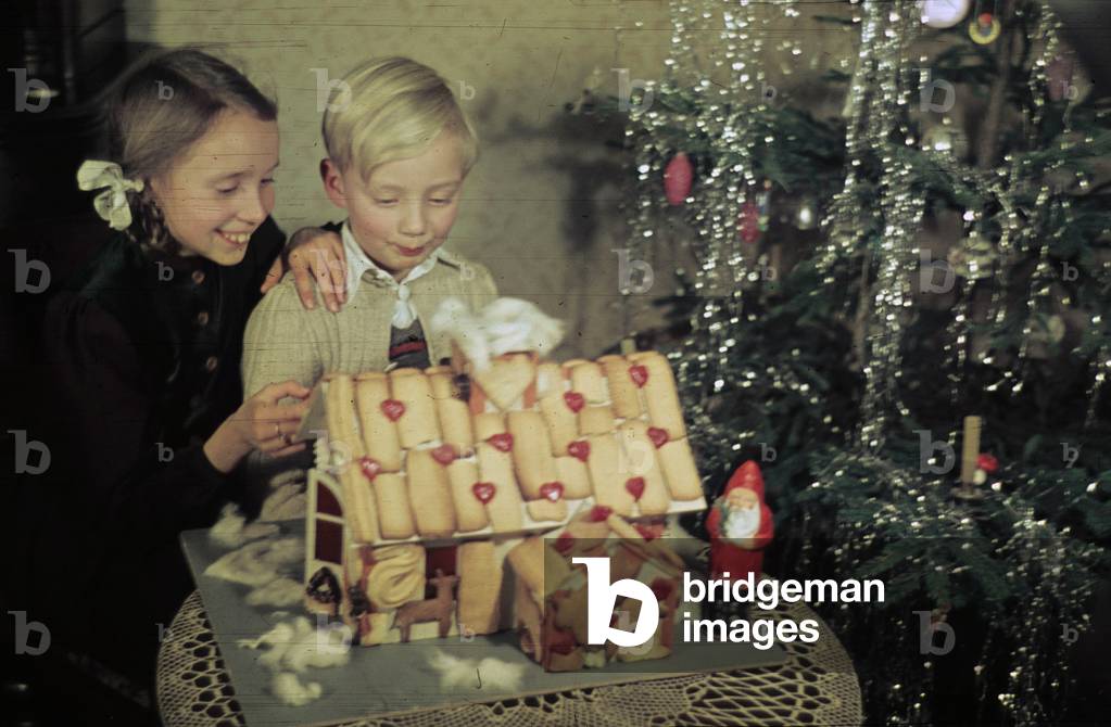 Siblings eating a gingerbread house in front of the Christmas tree on Christmas Eve, Merseburg, 1947 (photo)