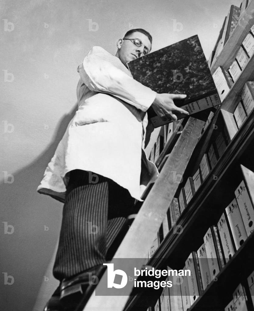Office worker organizing filing shelves, 1935 (b/w photo)