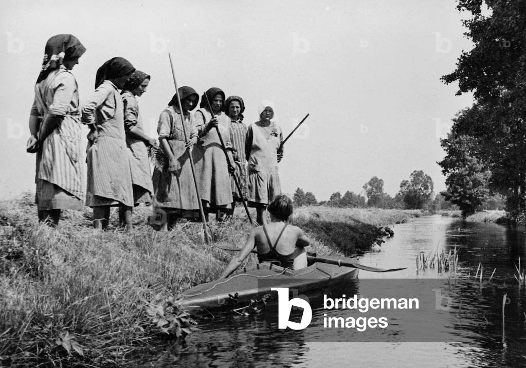 Farm workers examine a woman in folding kayak, 1931 (b/w photo)