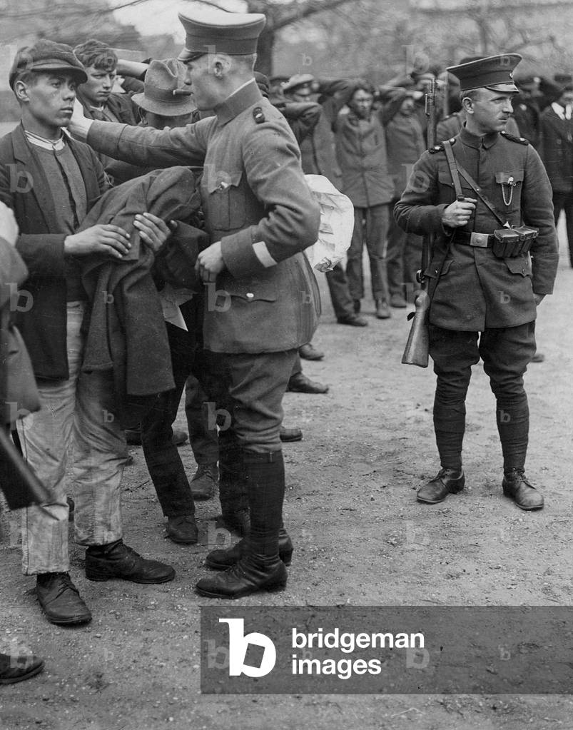 Policemen go through the pockets of looters, 1919 (b/w photo)