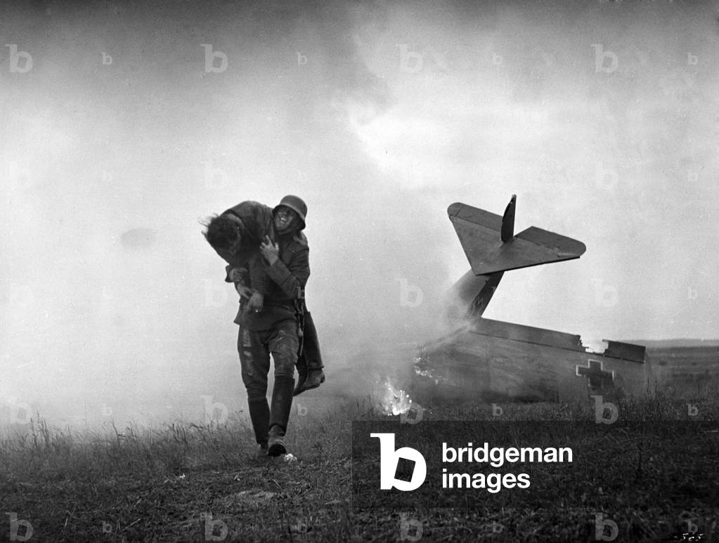 An infantryman carries an injured pilot from a German fighter plane that crashed on the Western Front. Probably film image, 1914 (b/w photo)