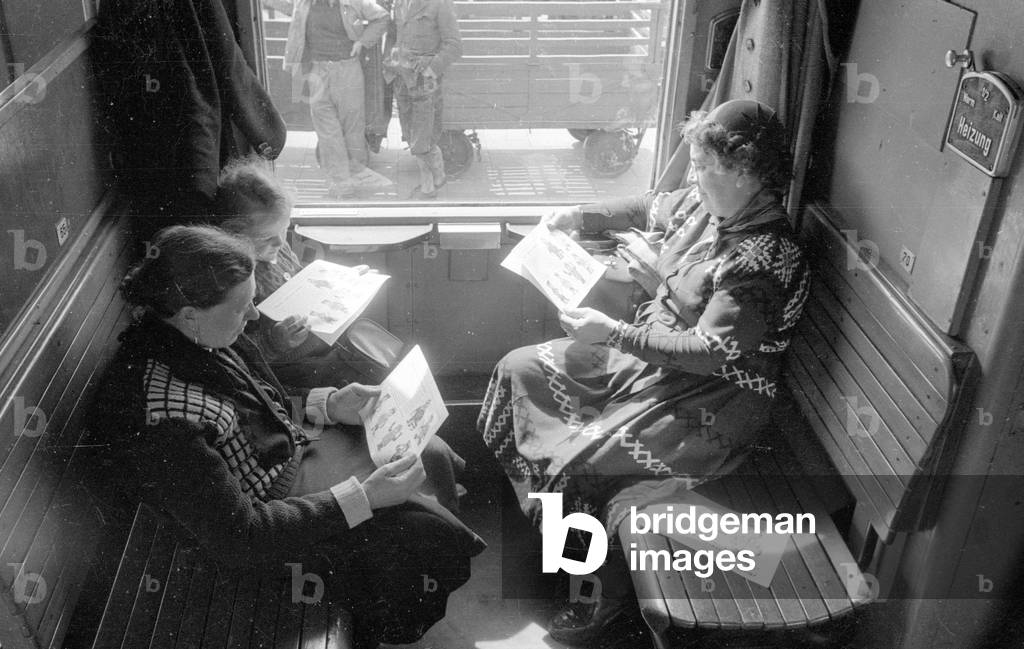 Train passengers with brochures in a train compartment, 1954 (b/w photo)