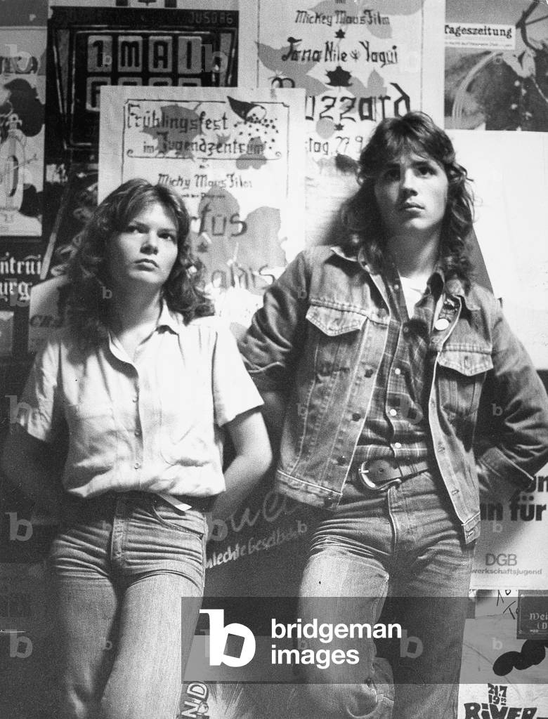 Two teenagers leaning against a wall with concert and event posters, 1981 (b/w photo)