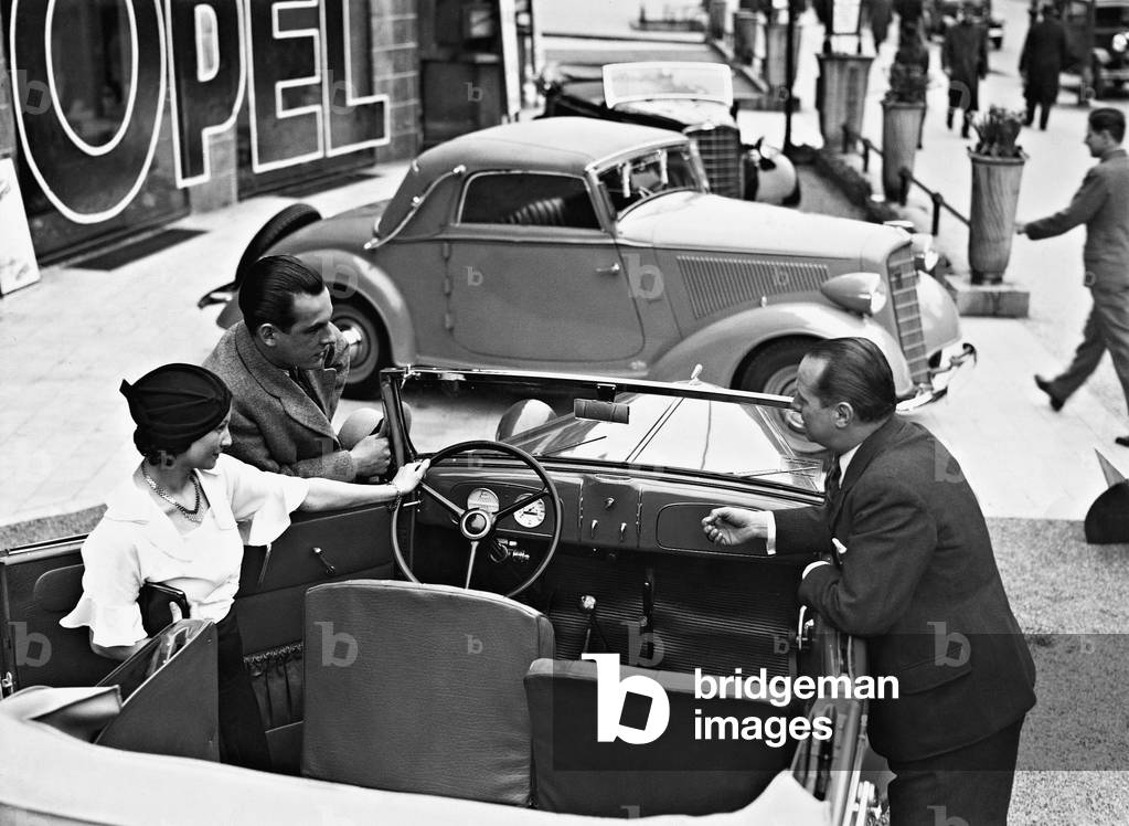 A car salesman and a young couple in a car dealership, 1935 (b/w photo)