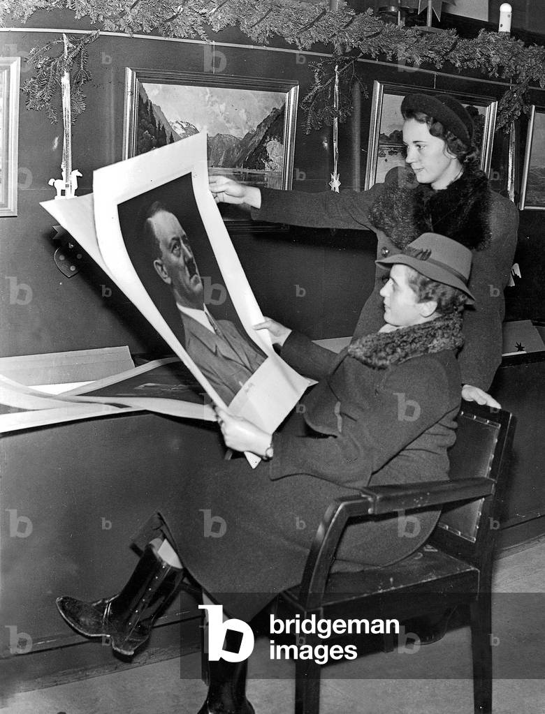 Two women looking at illustrations, including a portrait of Hitler, 1937 (b/w photo)