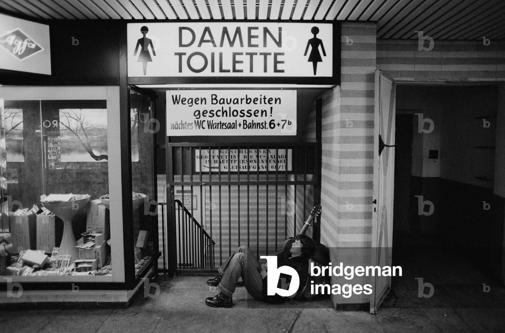 Street musician in front of a women's restroom (b/w photo)