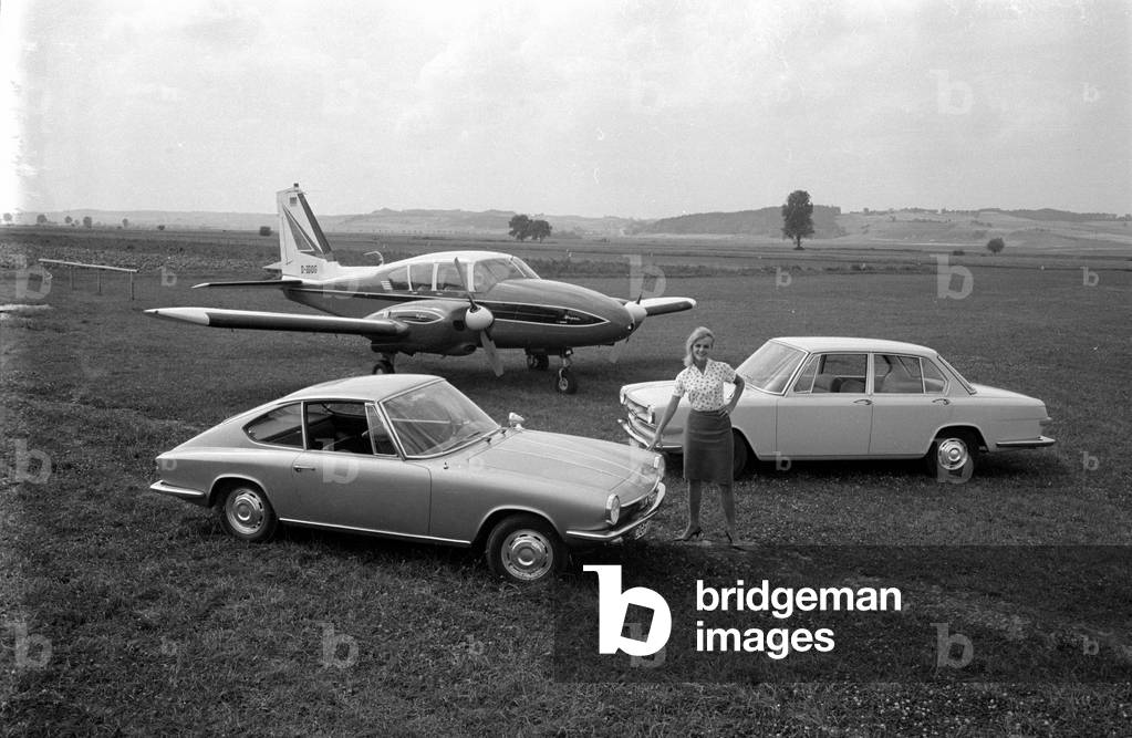 A woman posing with two cars in front of a light aircraft, 1963 (b/w photo)