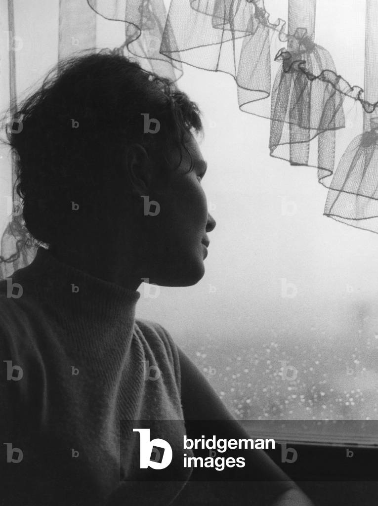 Young woman looks dreamily through rain-soaked windowpane, 1950s (b/w photo)