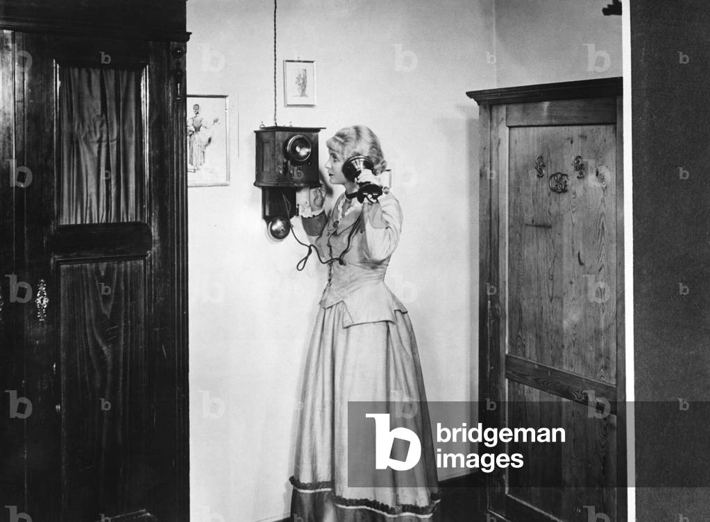 Woman making a phone call on a wall phone, 1882 (b/w photo)