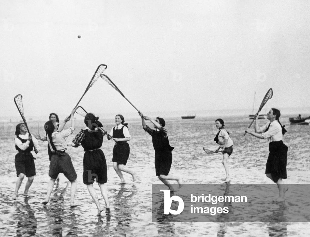 Girls playing lacrosse on the beach, 1912 (b/w photo)