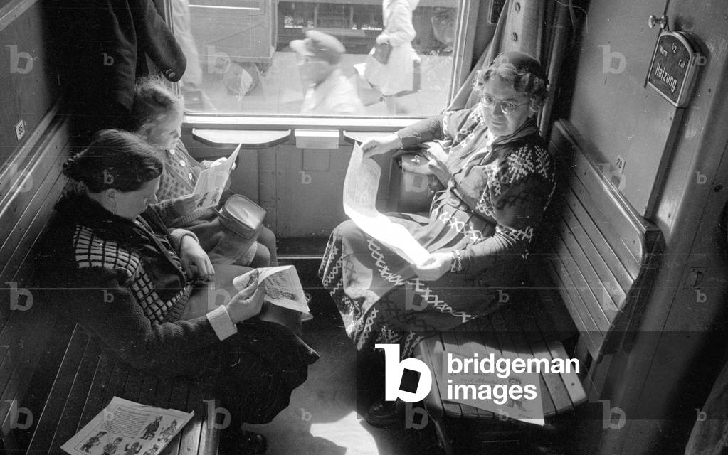 Train passengers with brochures in a train compartment, 1954 (b/w photo)