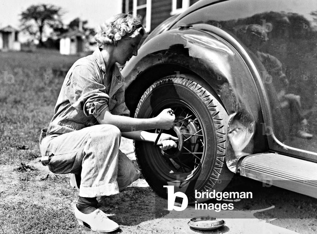 Woman changing a tire, 1937 (b/w photo)