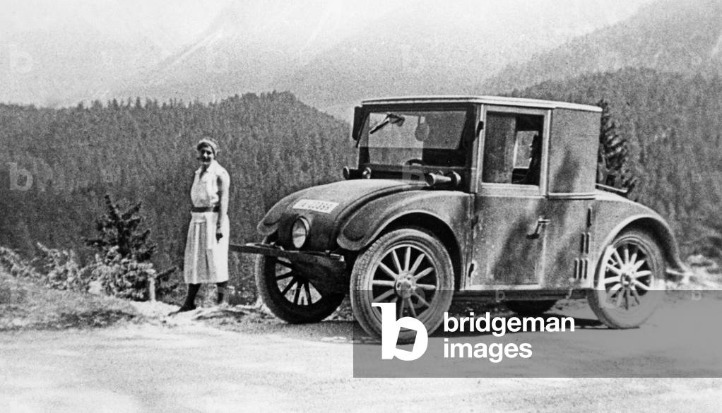 Vacationer next to small car on a mountain road, around the 1920s