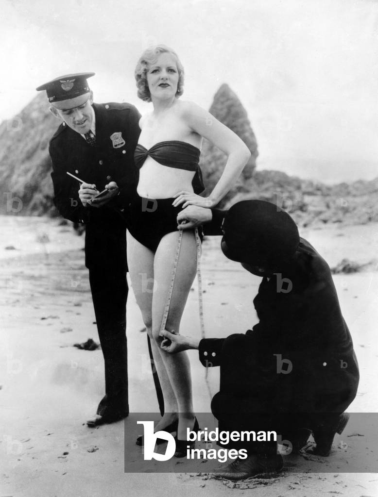 Policemen measuring Peggy Graves's swimming costume, to check whether it meets minimum clothing requirements, 1933 (b/w photo)