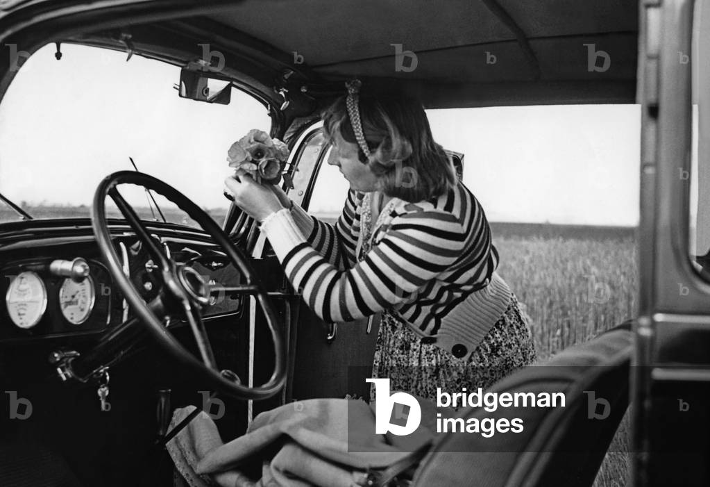 Woman putting a bouquet of flowers on the dashboard of her car, 1939 (b/w photo)