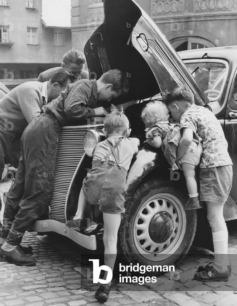 Young men inspecting a car motor, 1950 (b/w photo)
