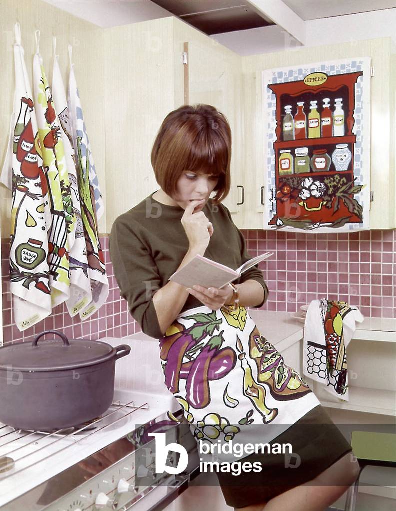 Woman in her kitchen reading a cookery book,, 60's
