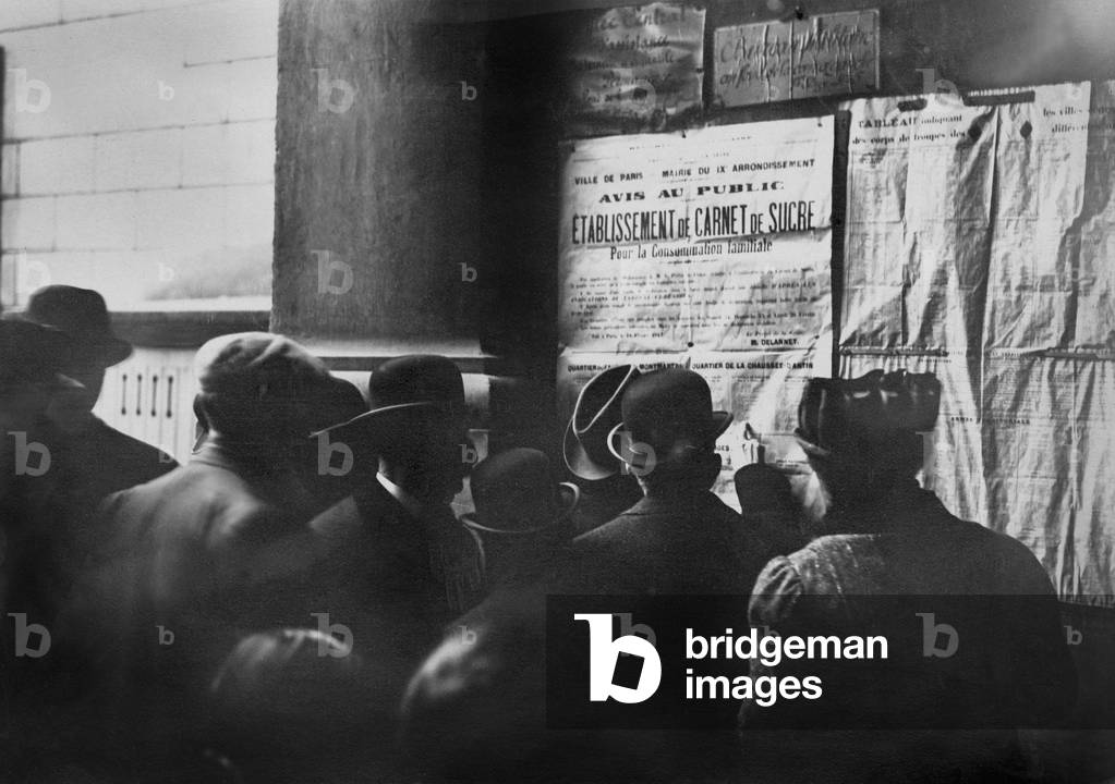 A group of French consults a posting of information on the food restrictions on sugar between 1914-1918