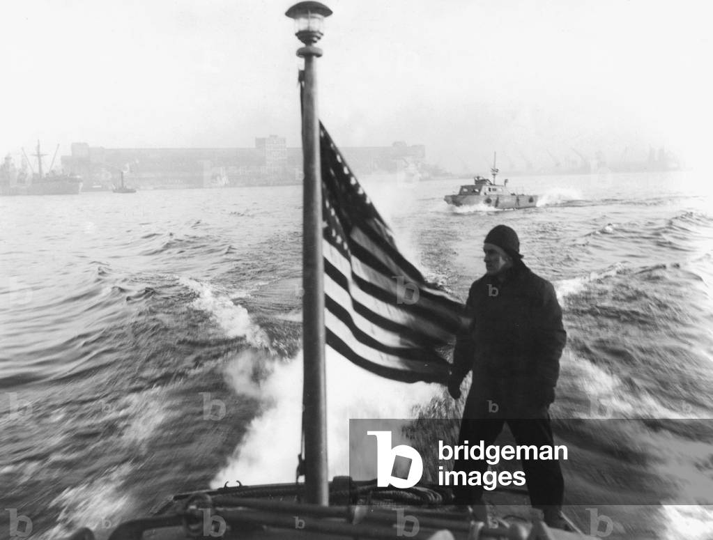 PVT Norbert Hust, rides on the stern of an army J-boat patrolling the harbor of Antwerp, Belgium in december 1944