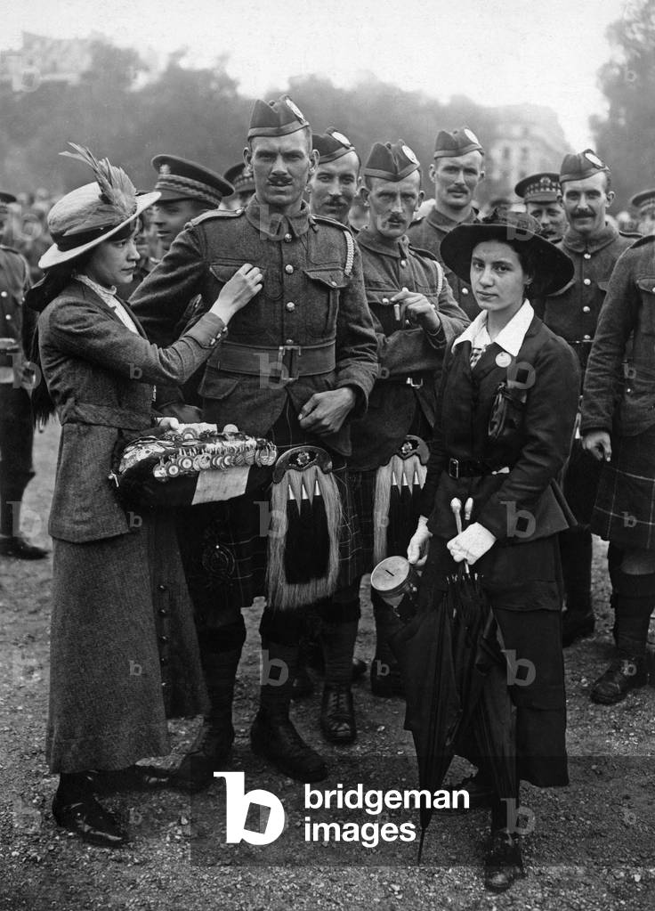 On july 14, 1916 in paris : a woman is giving decoration to scottish soldiers while another one takes the collection for works of war