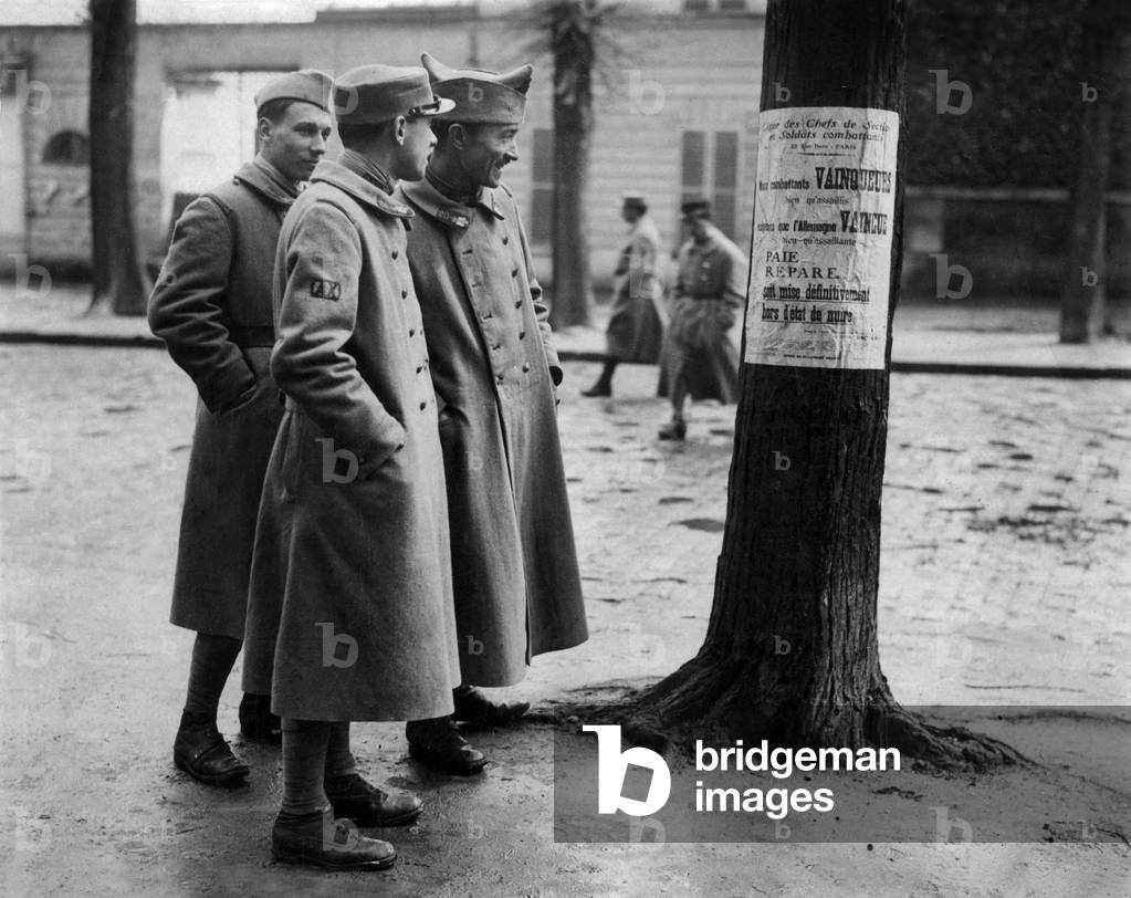 French soldiers reading a poster demanding that Germans pay for repairs after war, 1918