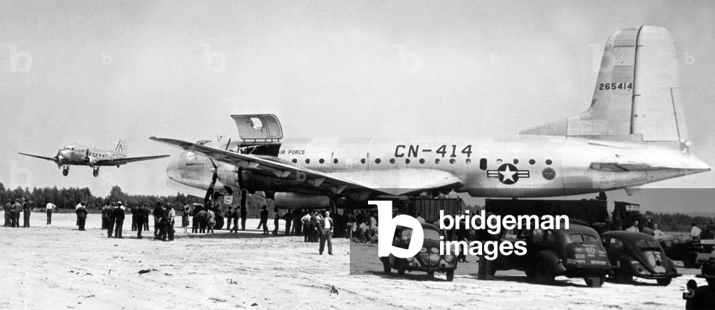 A C-74 plane, used by US Air Force in supplying Berlin, 1948. On left is a british Royal Air Force dakota airplane which is going to land at the nearby Gatow Air base