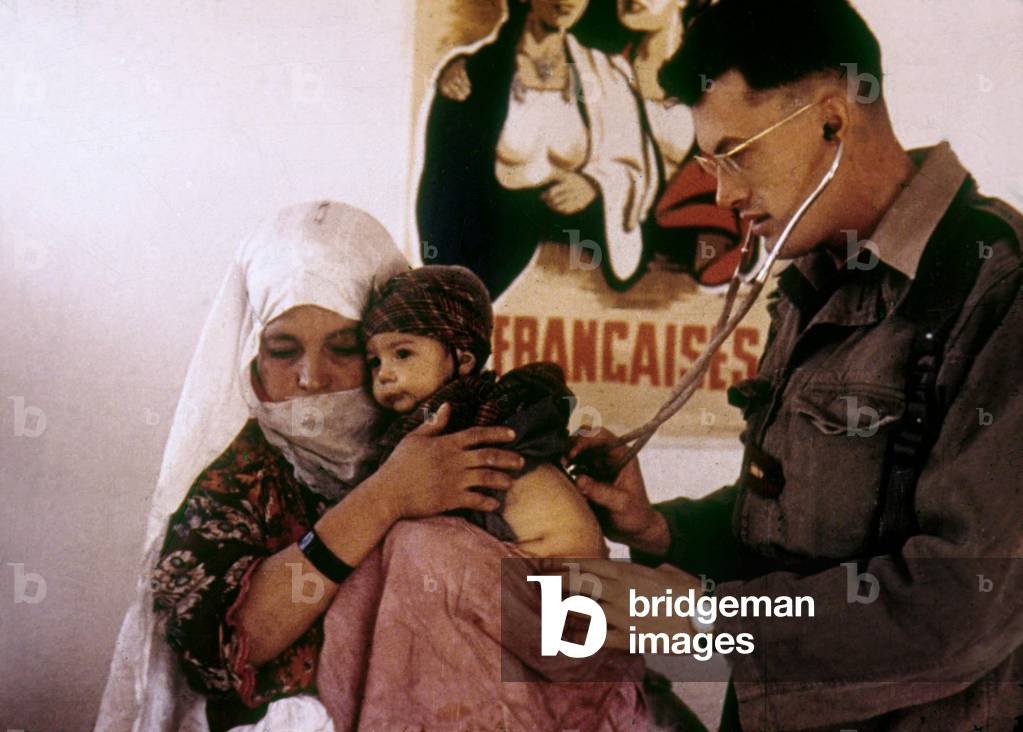 In a village in Algeria at time of war (1954-1962) an army doctor examining a child in arms of his mother