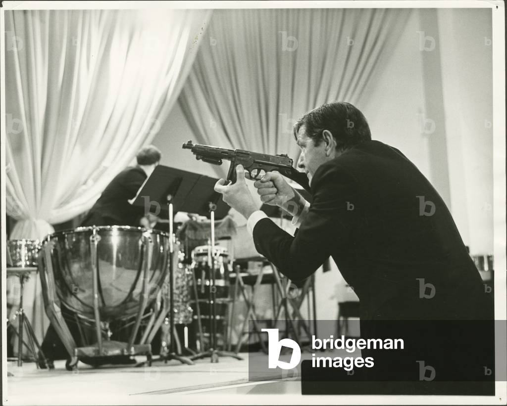 John Cage with gun during performance of David Rosenboom's 'To That Predestined Dancing Place' at Albright-Knox Art Gallery performance for the 2nd Festival of the Arts