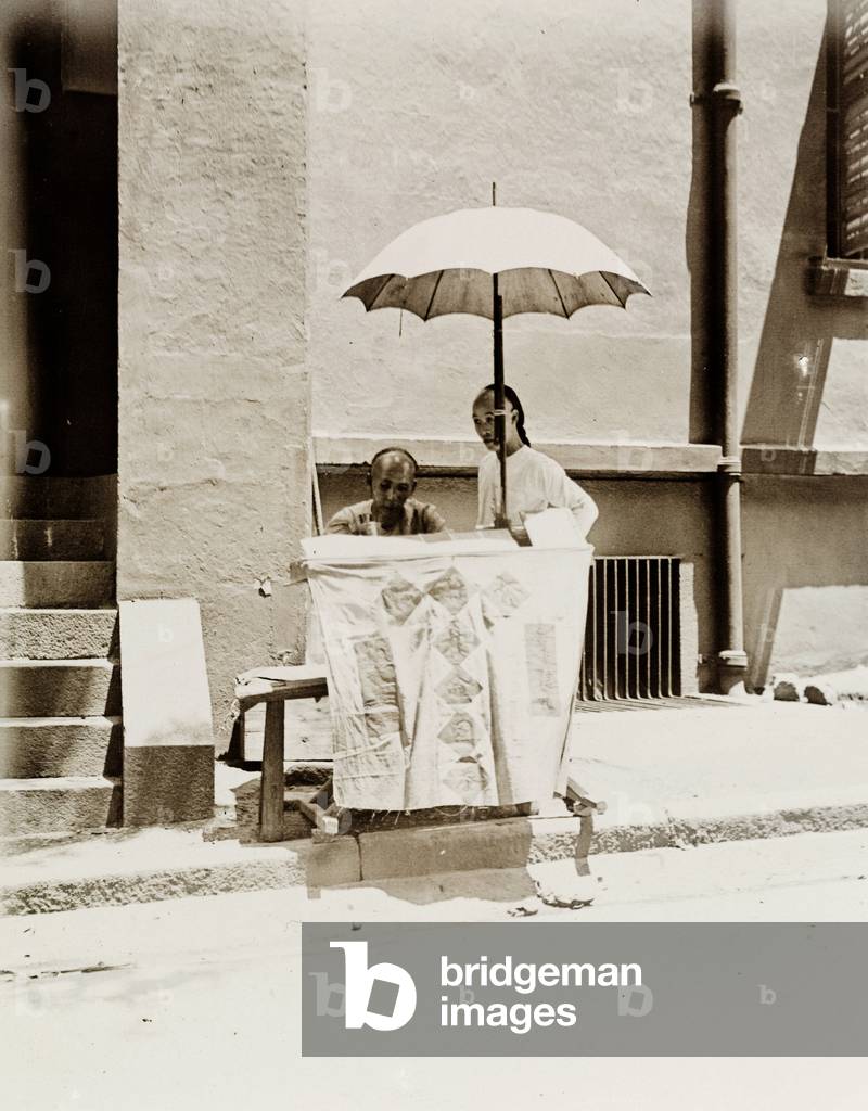 Un venditore ambulante che offre un servizio di scrittura di lettere siede sotto un ombrellone nella sua banca