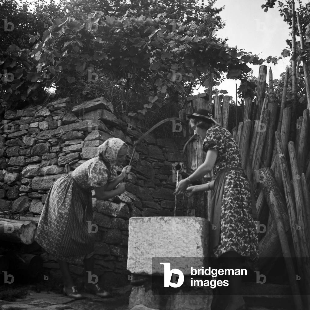 Two young women wearing countryside fashion at a well in an old courtyard, Austria 1930s (b/w photo)