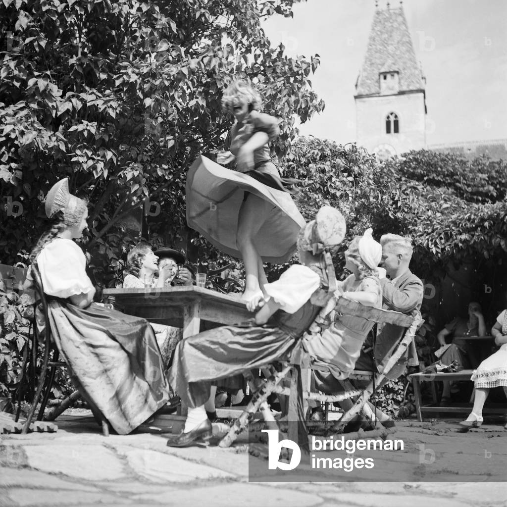 A young woman tasting the wine of the Wachau area in Austria and dancing on the table, Germany 1930s (b/w photo)