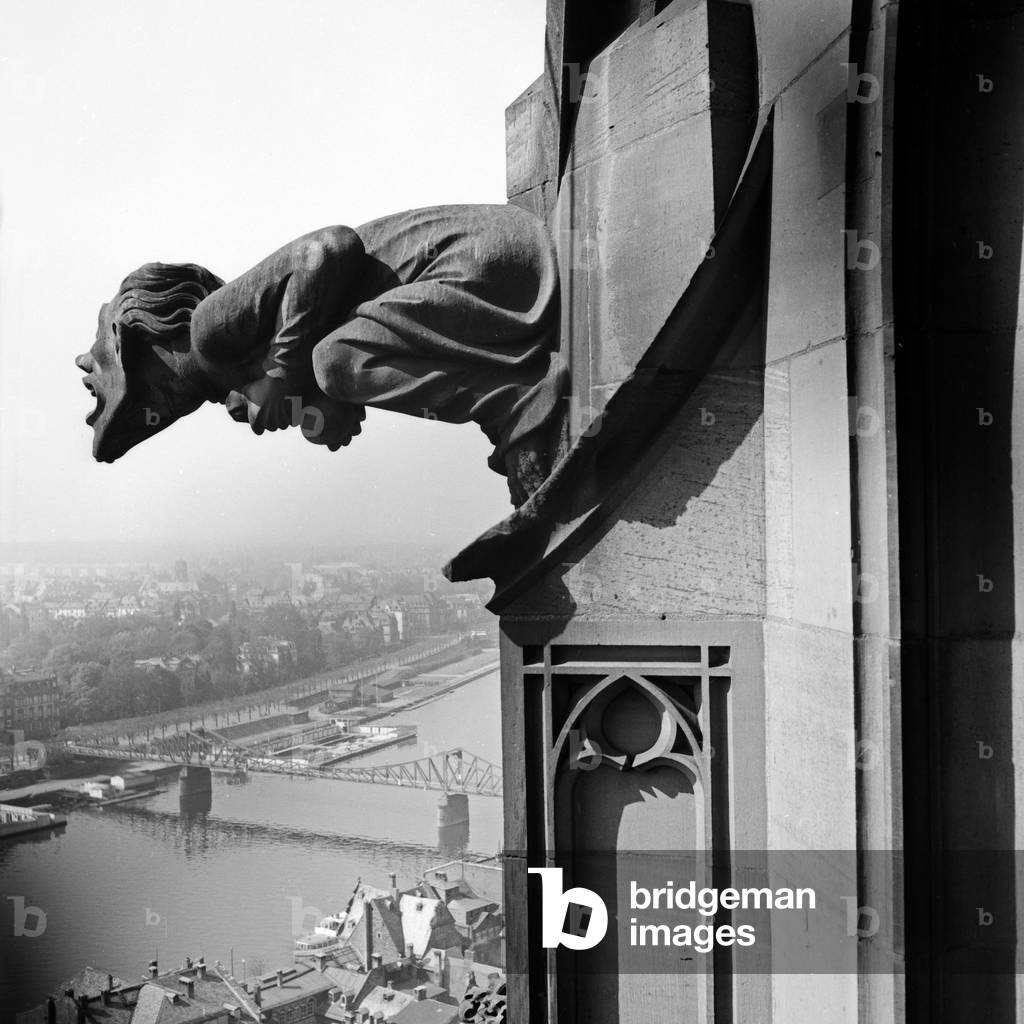 A gargoyle at the belfry of St Bartolomew's cathedral watching over the city of Frankfurt, Germany 1930s (b/w photo)