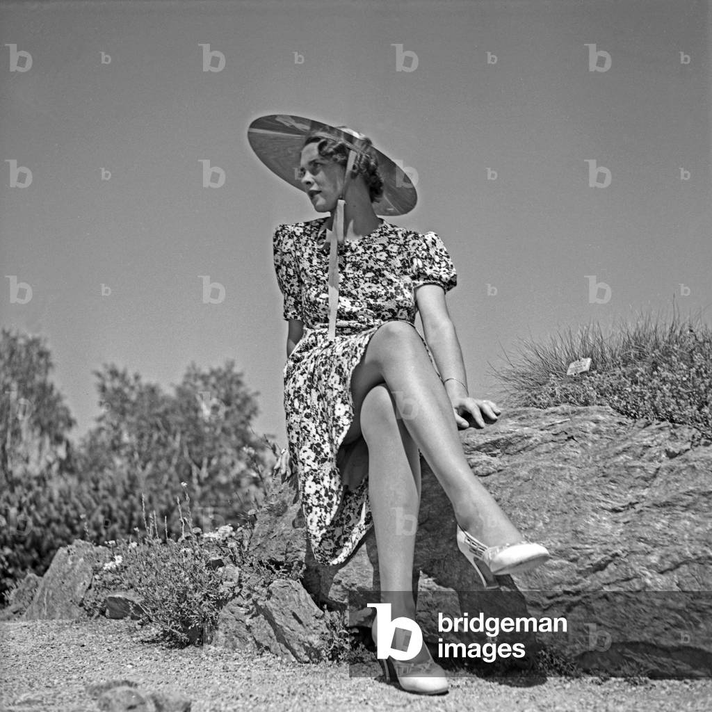 A young woman wearing a summer dress sitting on a rock, Deutschland 1930s (b/w photo)