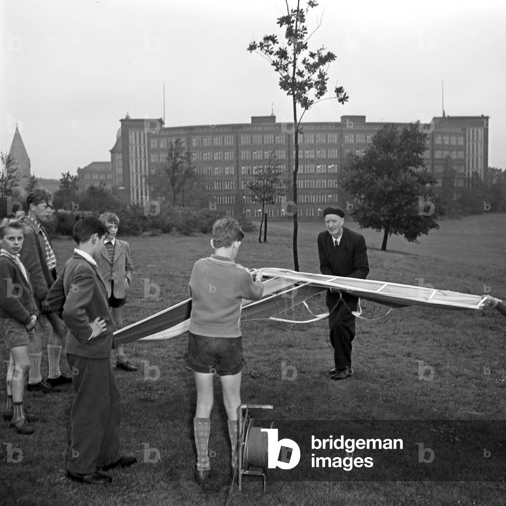 An elder man flying a kite with some children, Germany 1950s