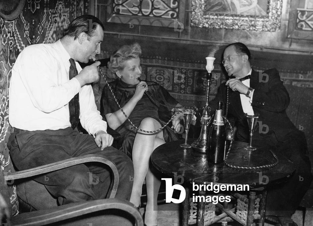 Guests of a nightclub at Hamburg Reeperbahn enjoy their hooka pipe and a glass of sparkling wine, 1950s