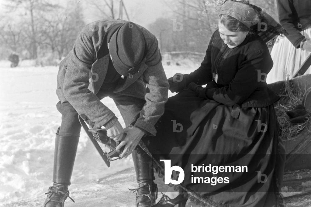A man helping a woman to put on ice skate runners at Spreewald area, Germany 1930s (b/w photo)