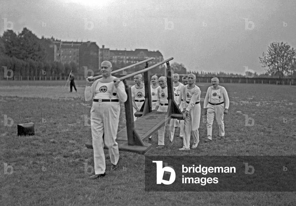 Senior department of a gymnastic club carrying uneven bars on a sporting ground, Germany 1930s (b/w photo)