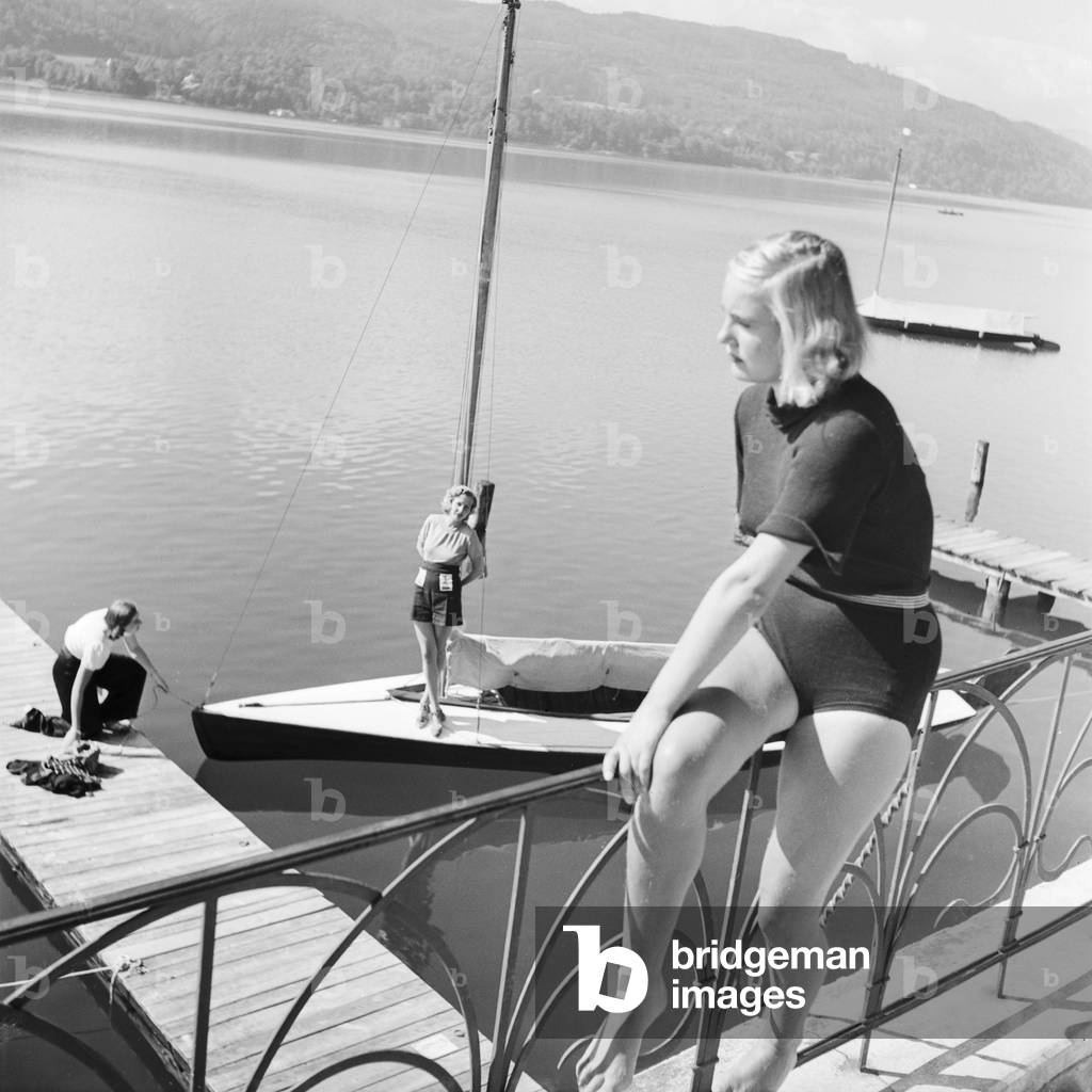 A young woman sitting on a railing at a lake in the Wachau area in Austria, Germany 1930s (b/w photo)
