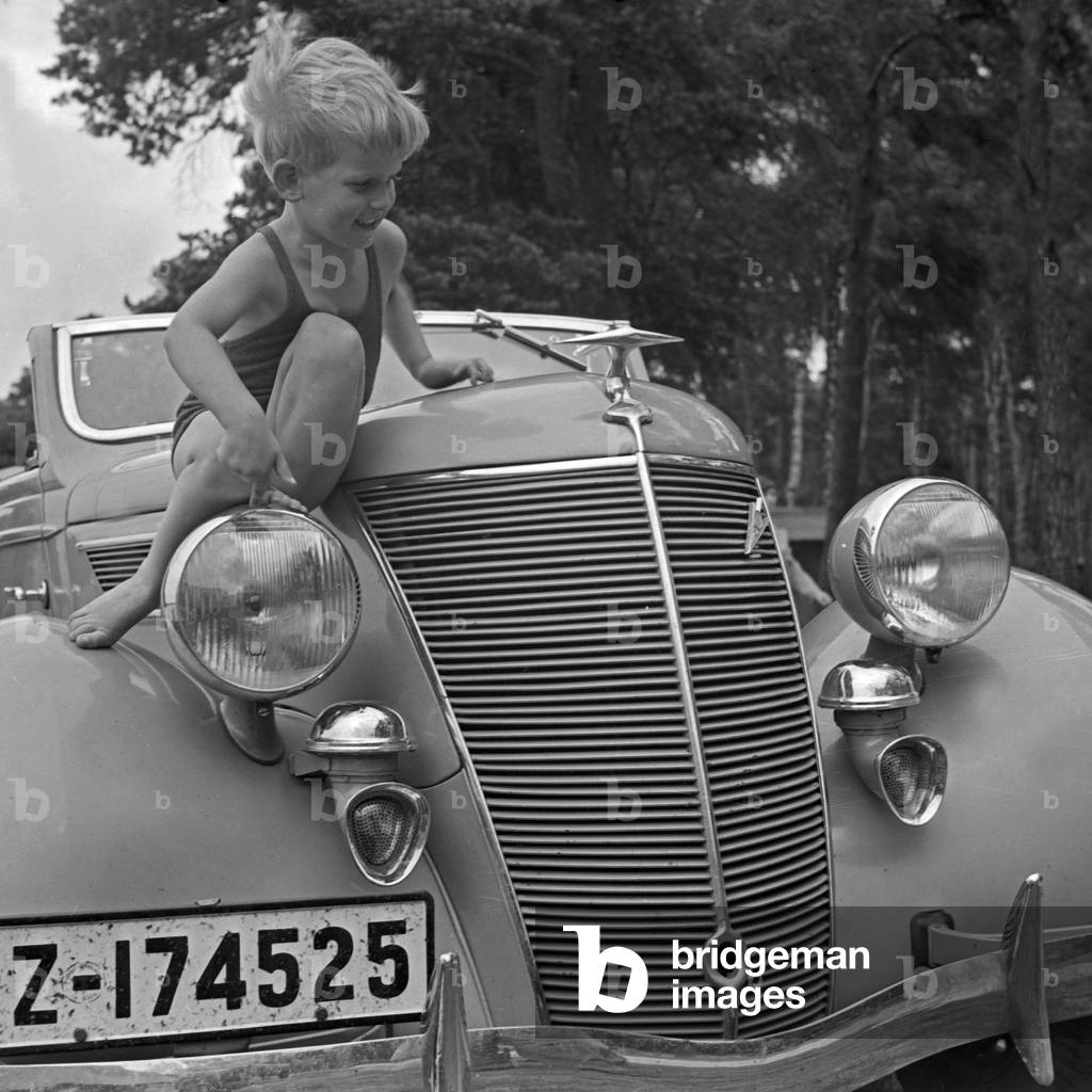 A little boy playing on the bonnet of a Ford V8 convertible, Germany 1930s (b/w photo)