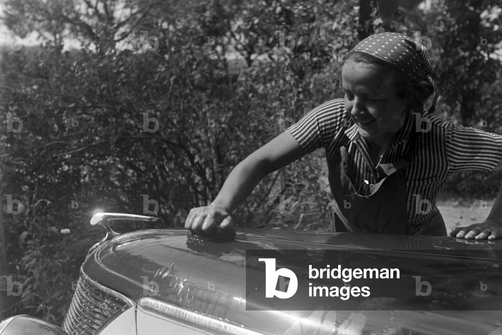 A young woman washing a Ford model Eifel, Germany 1930s (b/w photo)