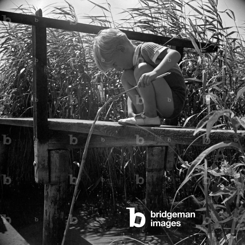 A little boy, lost in thoughts, playing at a grouser, Germany 1930s (b/w photo)