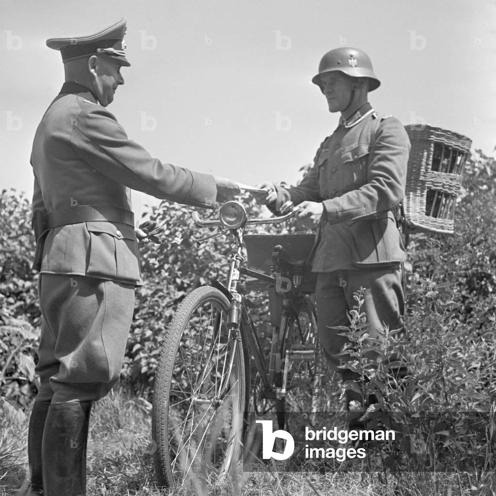 A signal corps officer giving a message to the bicyclist of the carrier pigeon unit for forwarding it via pigeon to the frontline, Germany 1940s (b/w photo)