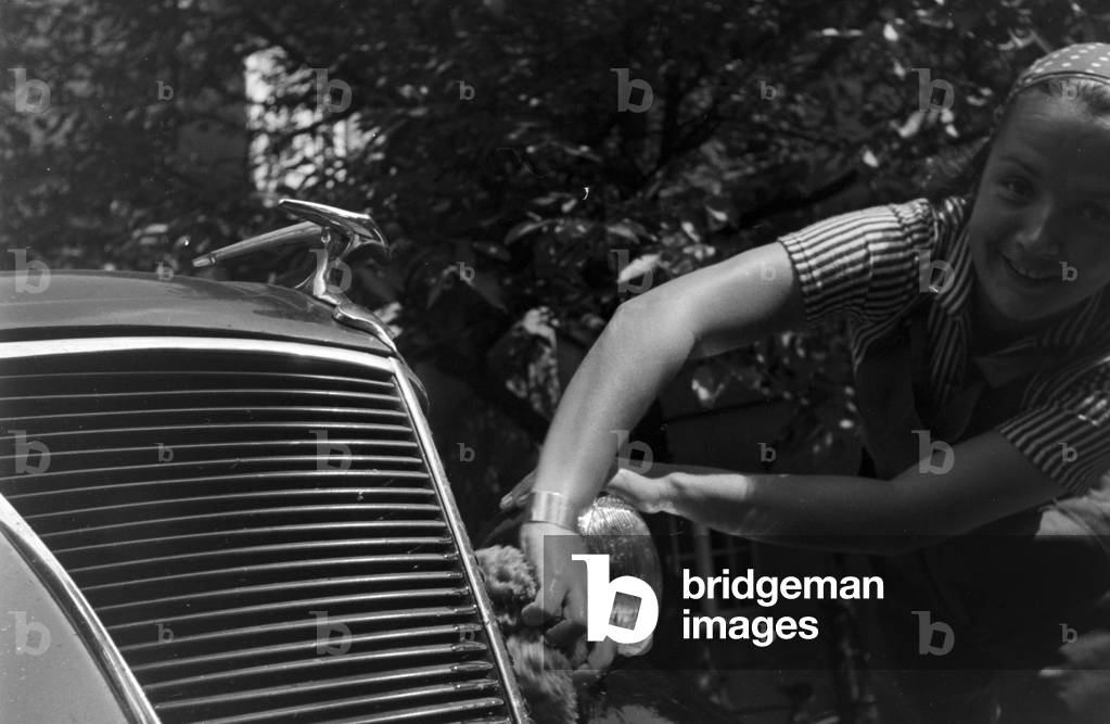 A young woman washing a Ford model Eifel, Germany 1930s (b/w photo)